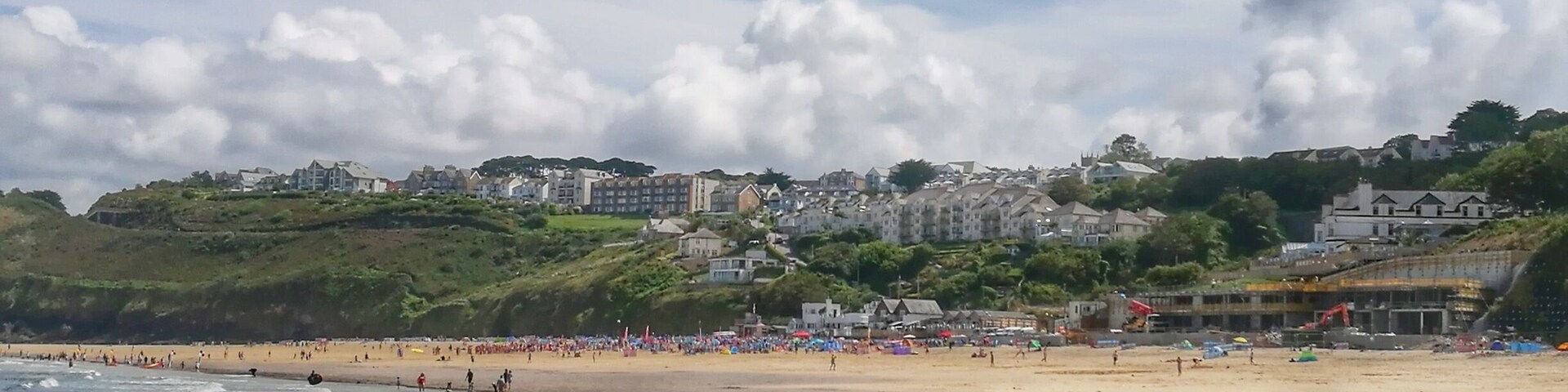 Una playa con olas, gente y edificios al fondo.