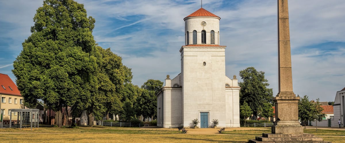 A church with a tall tower and a large tree in front.