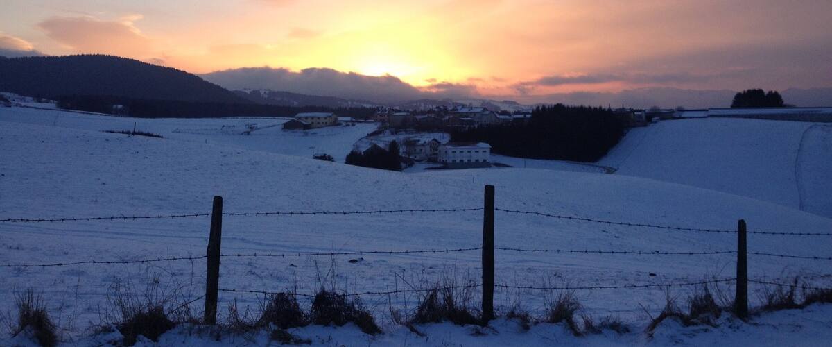 A snowy landscape with a sunset, a barbed wire fence, and a small building in the distance.