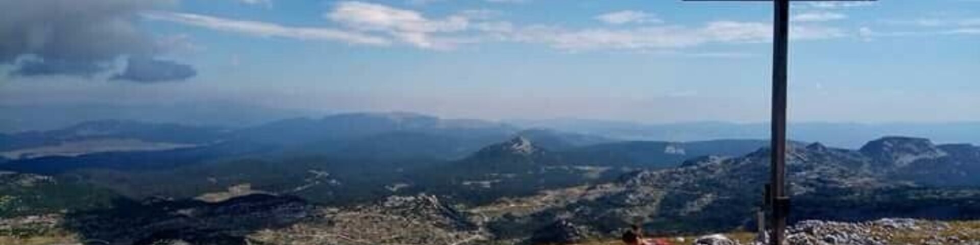 Une croix au sommet d’une colline, offrant une vue panoramique sur les montagnes et les vallées lointaines.