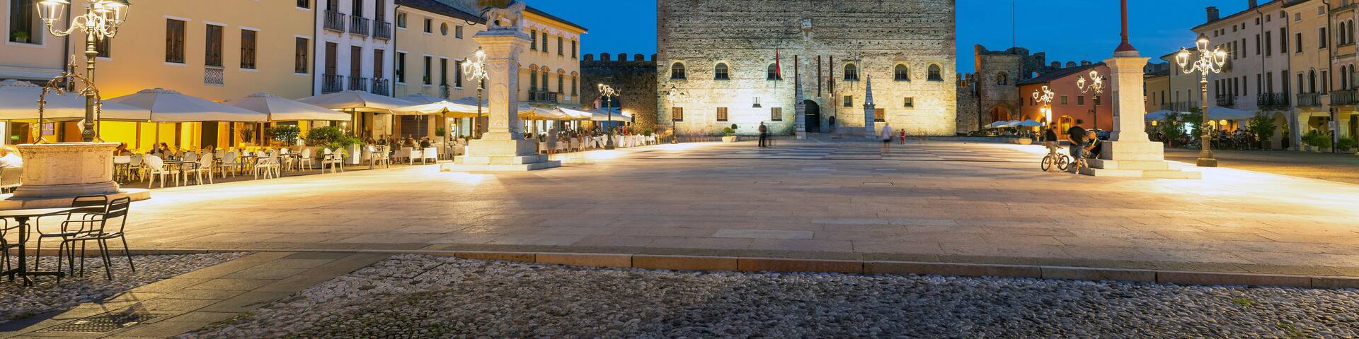 Marostica, Italy - Chess square in the evening. People sitting at the tables of the bars in the square. In the background the medieval castle