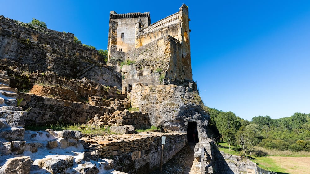 Un château de pierre historique, doté d’une tour, de ruines et surplombant un ciel d’un bleu limpide.