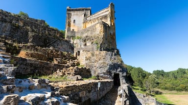 Un castillo de piedra histórico con una torre, ruinas y un cielo azul despejado.