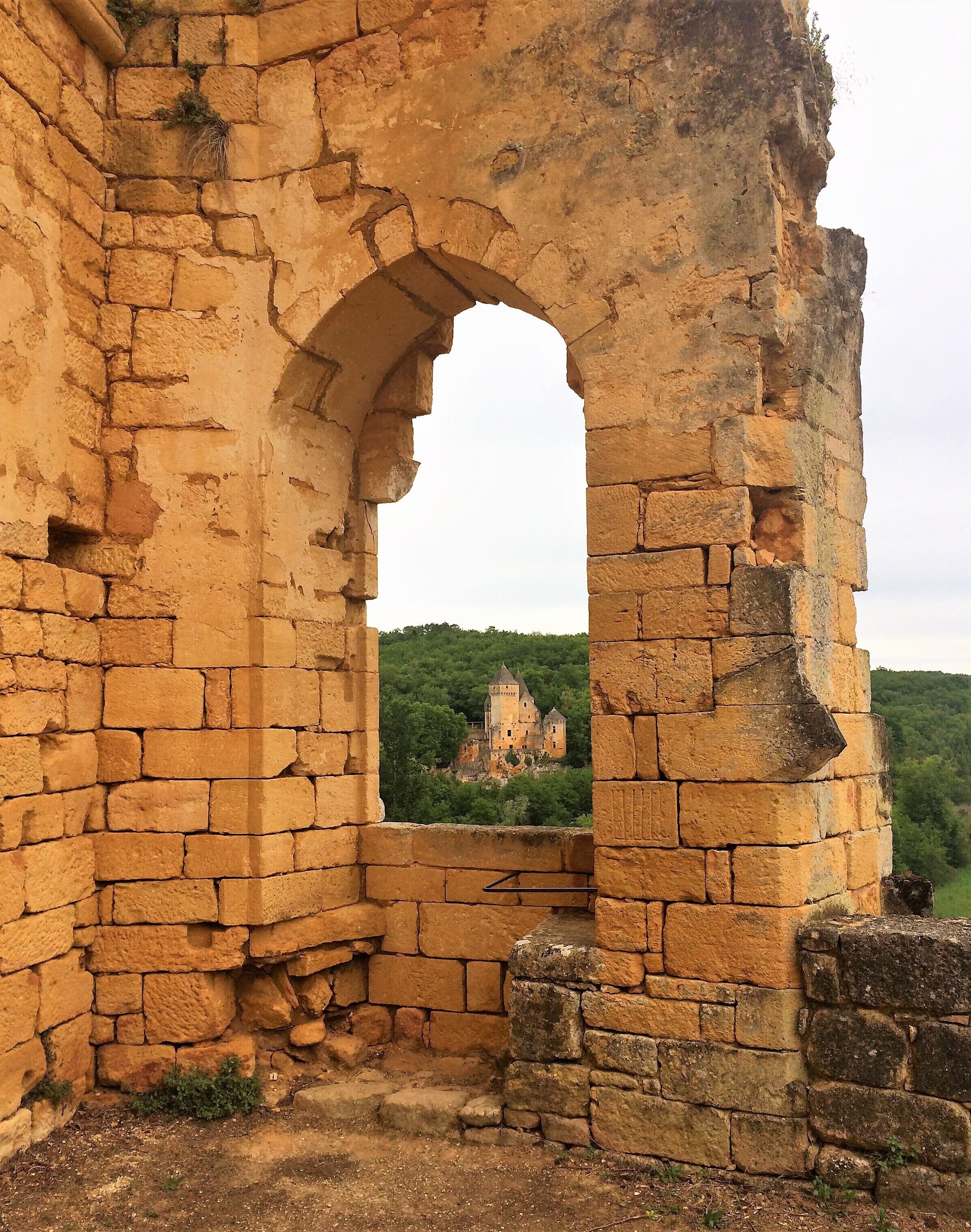 An ancient stone archway leading to a castle on a hill.