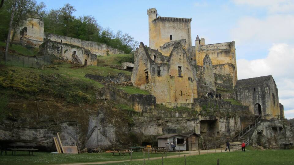 A historic castle with a prominent tower, situated on a grassy hill with a clear sky.