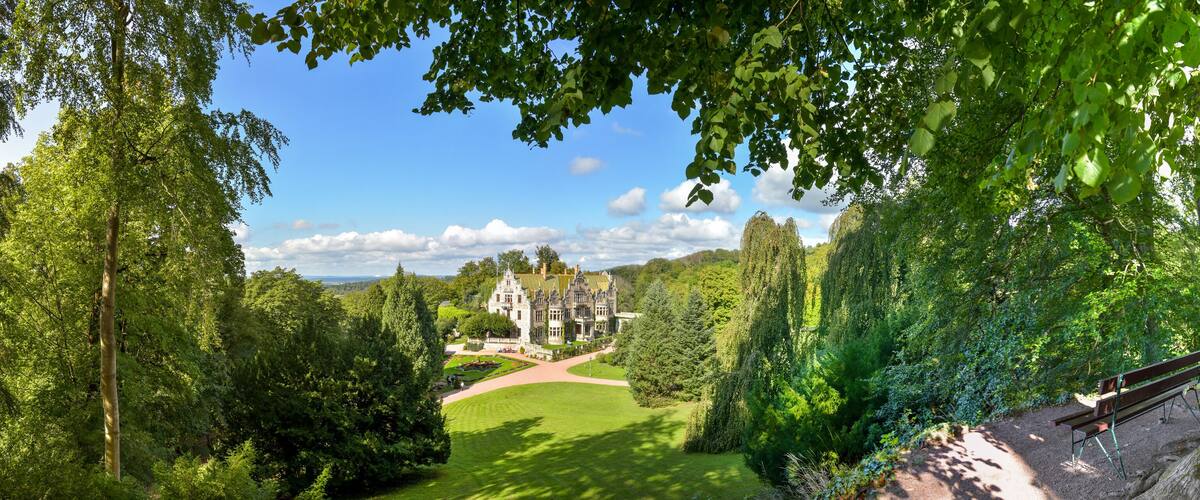 A large, historic building surrounded by lush greenery and a well-maintained lawn.