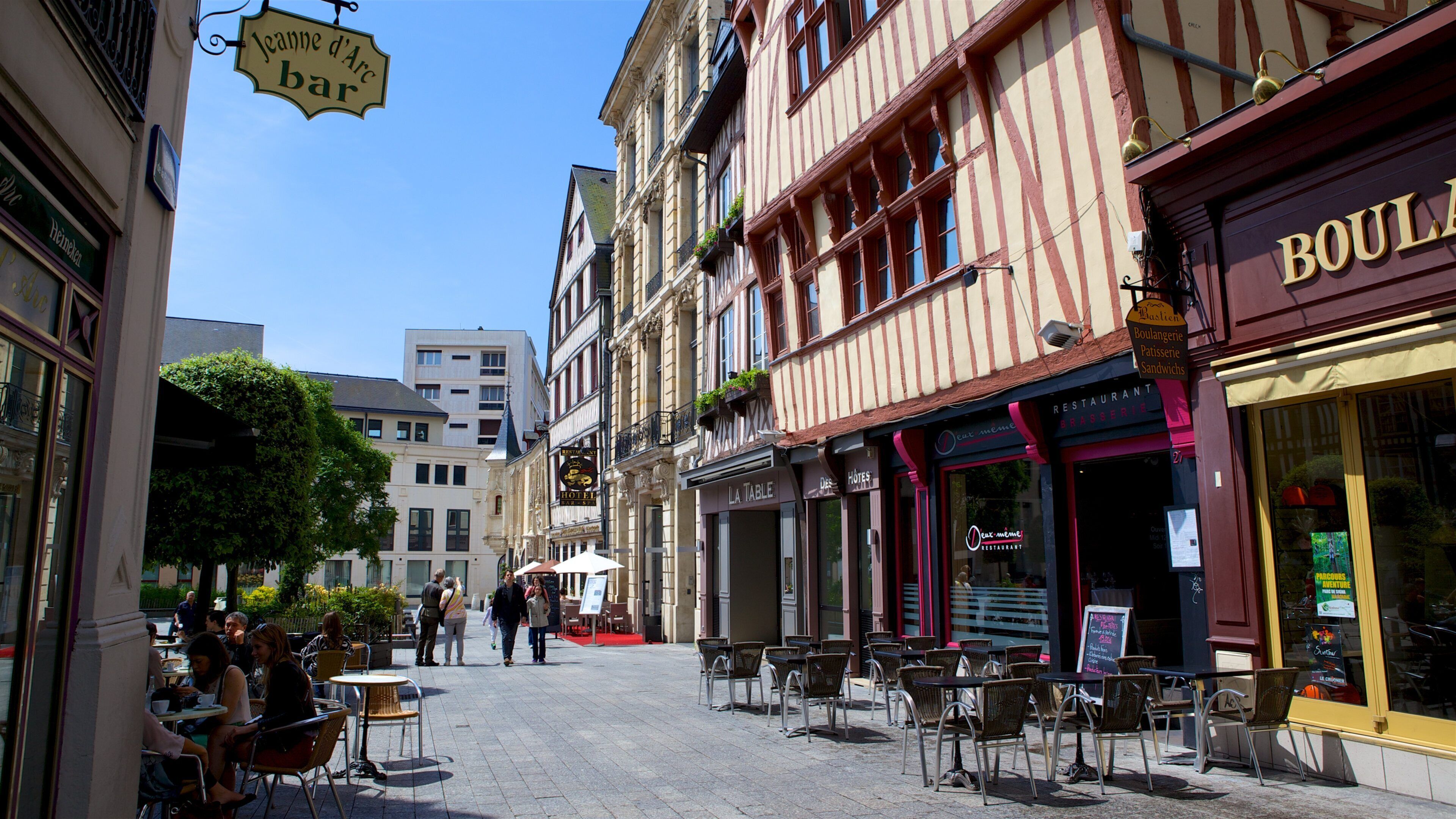 A cobblestone street lined with historic buildings, outdoor cafes, and a variety of shops.
