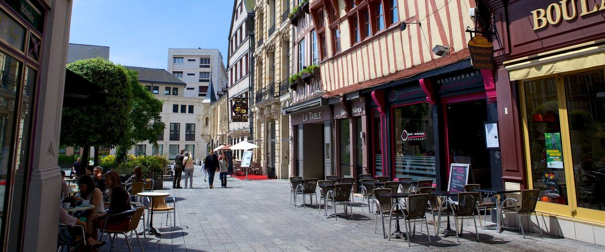 A cobblestone street lined with historic buildings, outdoor cafes, and a variety of shops.