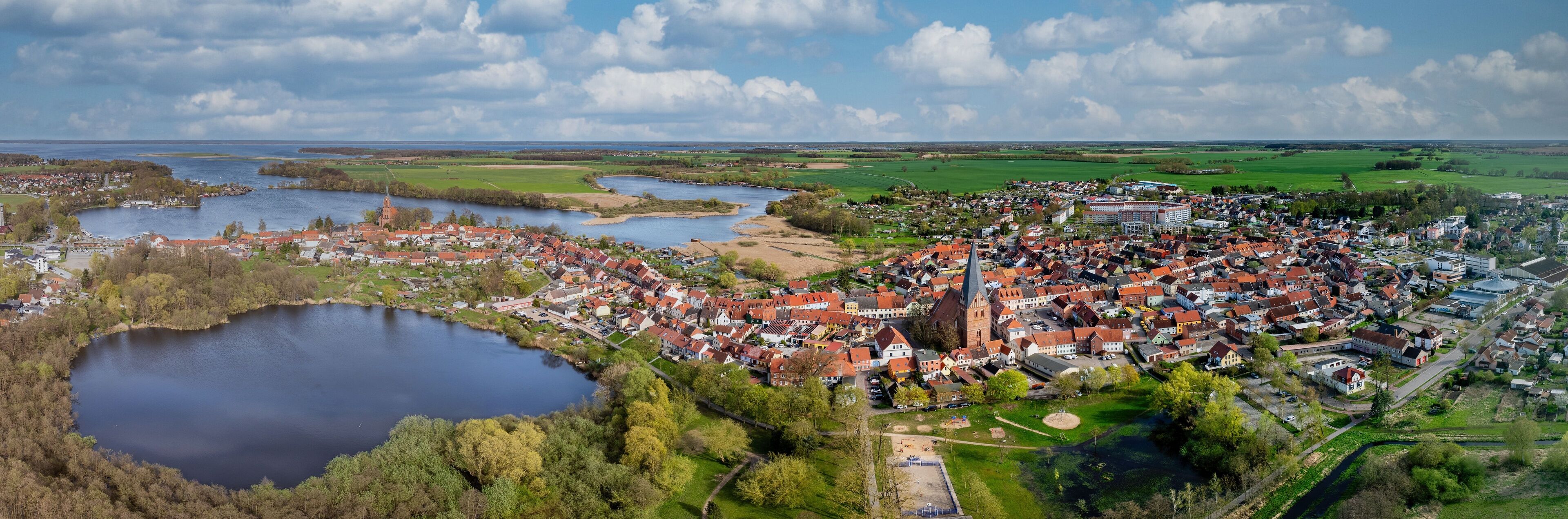 Eine Stadt mit einem zentralen Kirchengebäude, einem See und umliegenden Feldern.