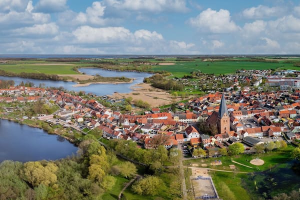 Eine Stadt mit einem zentralen Kirchengebäude, einem See und umliegenden Feldern.