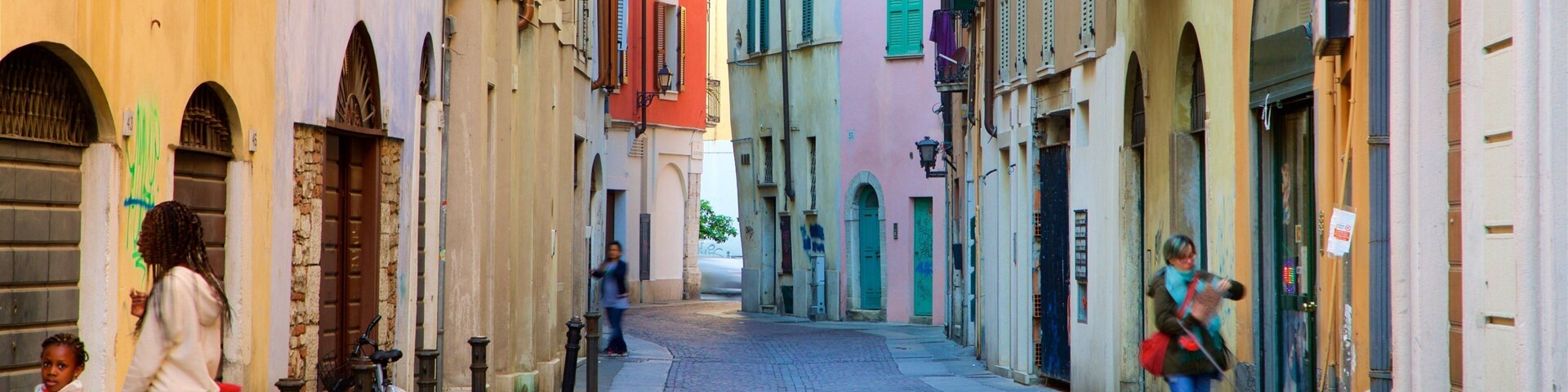 Uma rua de paralelepípedos estreita, ladeada por edifícios coloridos, uma bicicleta e pedestres.