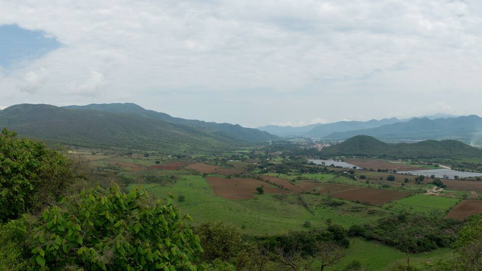 A valley with green fields, distant mountains, and a small settlement.