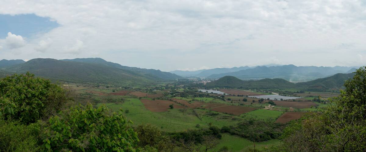 A valley with green fields, distant mountains, and a small settlement.