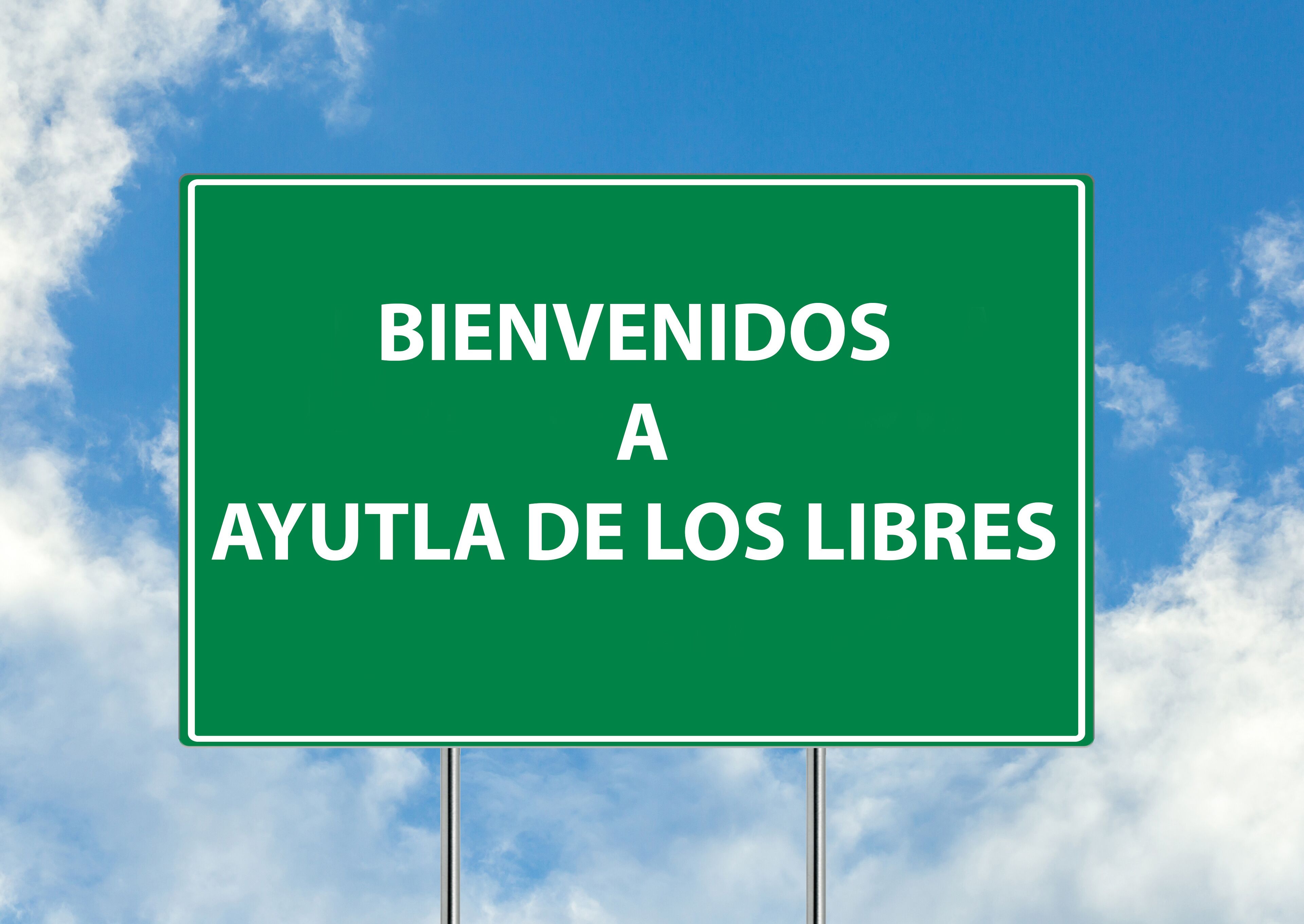 A green welcome sign with white text against a blue sky with clouds.