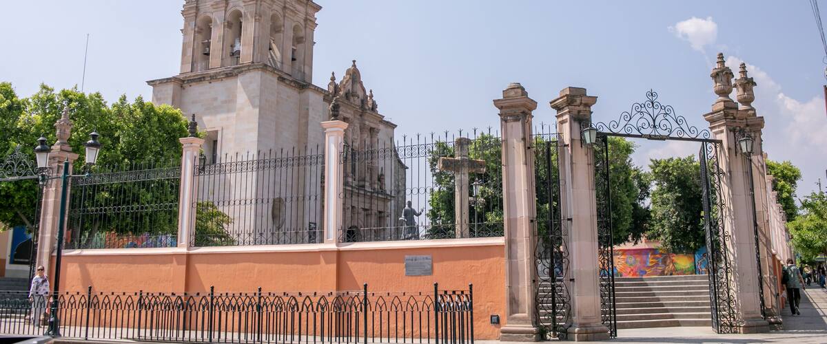 A historic church with a bell tower, a wrought iron gate, and a staircase leading to the entrance.
