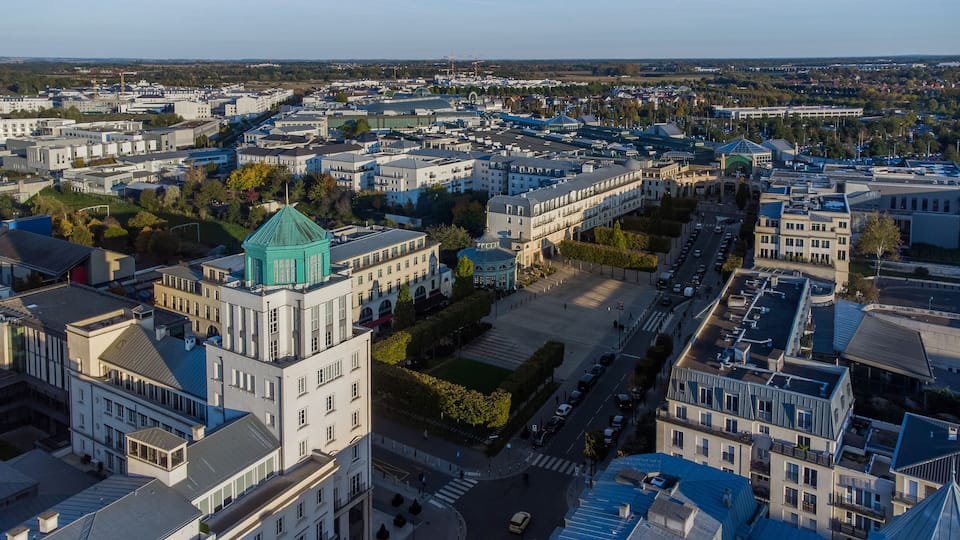 An aerial view of a city with historic buildings, a prominent green-roofed tower, and a large open square.