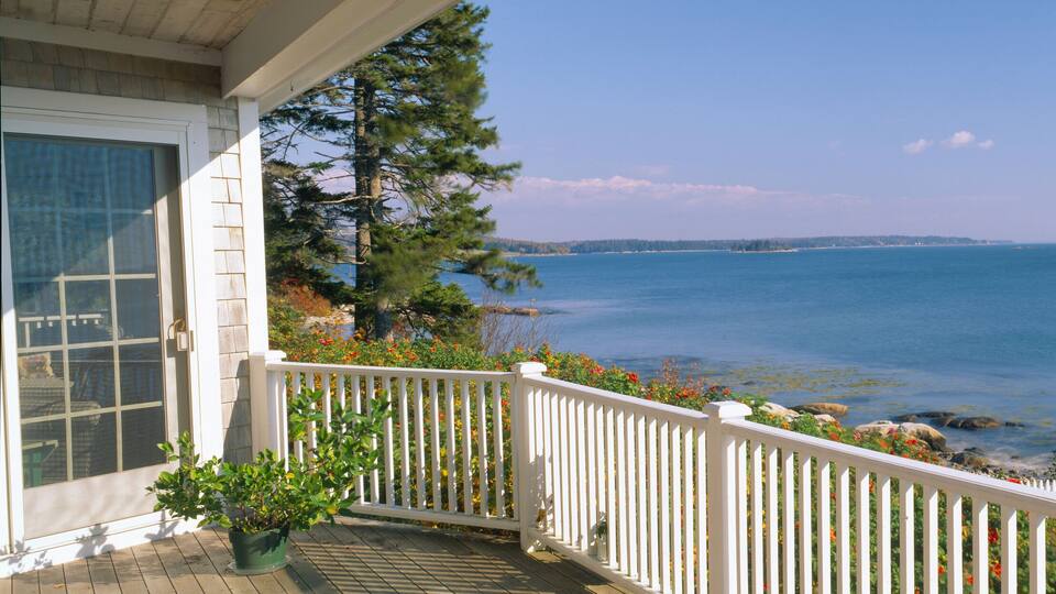 A coastal view with a wooden deck, white railing, and a clear blue sea.