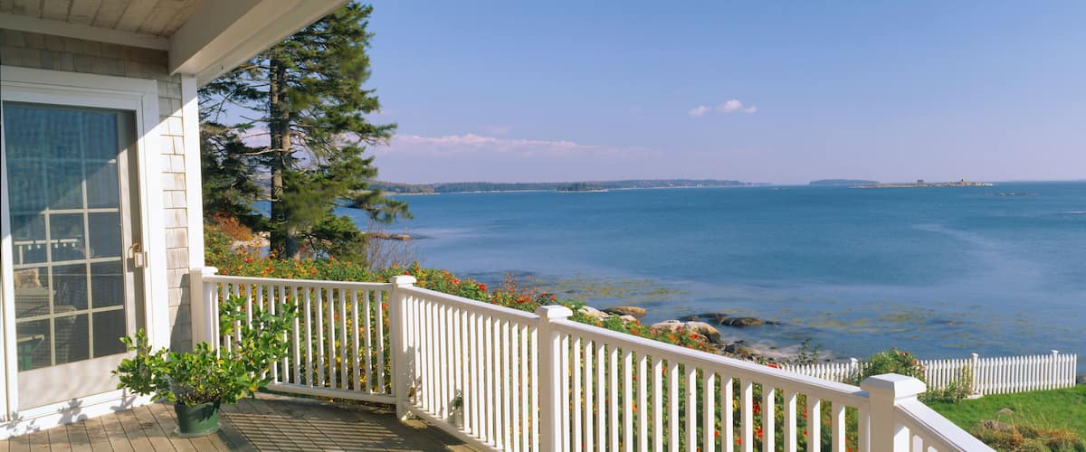 A coastal view with a wooden deck, white railing, and a clear blue sea.