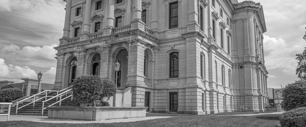 A large, classical building with columns and a triangular pediment, surrounded by a well-maintained lawn and a staircase leading to the entrance.