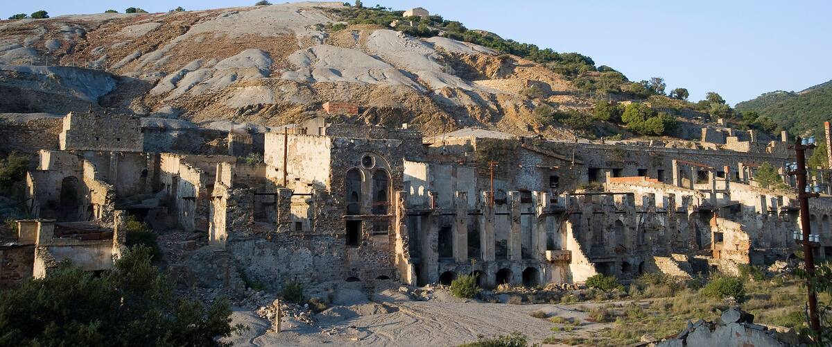 Ancient ruins with columns and arches, a hillside with sparse vegetation, and a clear blue sky.
