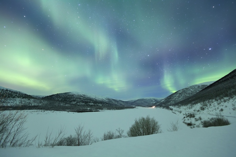 A snowy landscape with a starry night sky and the Northern Lights.