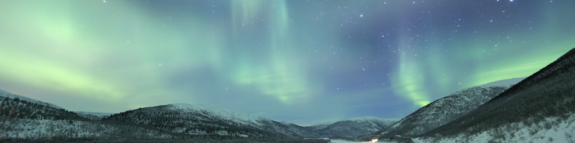 Eine verschneite Landschaft mit Sternenhimmel und Polarlichtern.