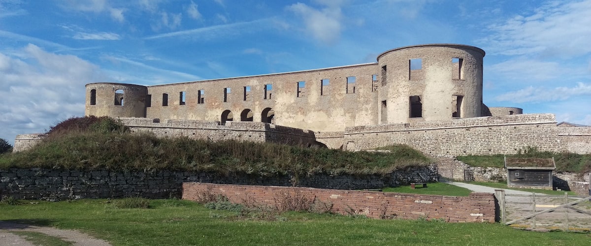 A historic stone castle with a round tower, surrounded by a grassy area and a stone wall.