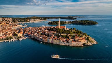 Un pueblo costero con una torre destacada, un puerto con barcos y una pequeña isla de vegetación densa.