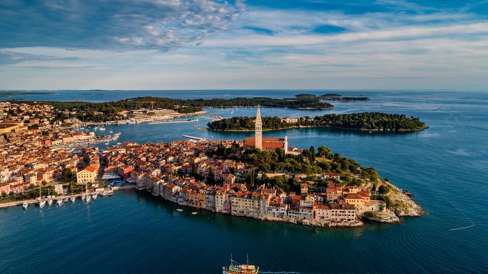 A coastal town with a prominent tower, a harbor with boats, and a small island with dense greenery.