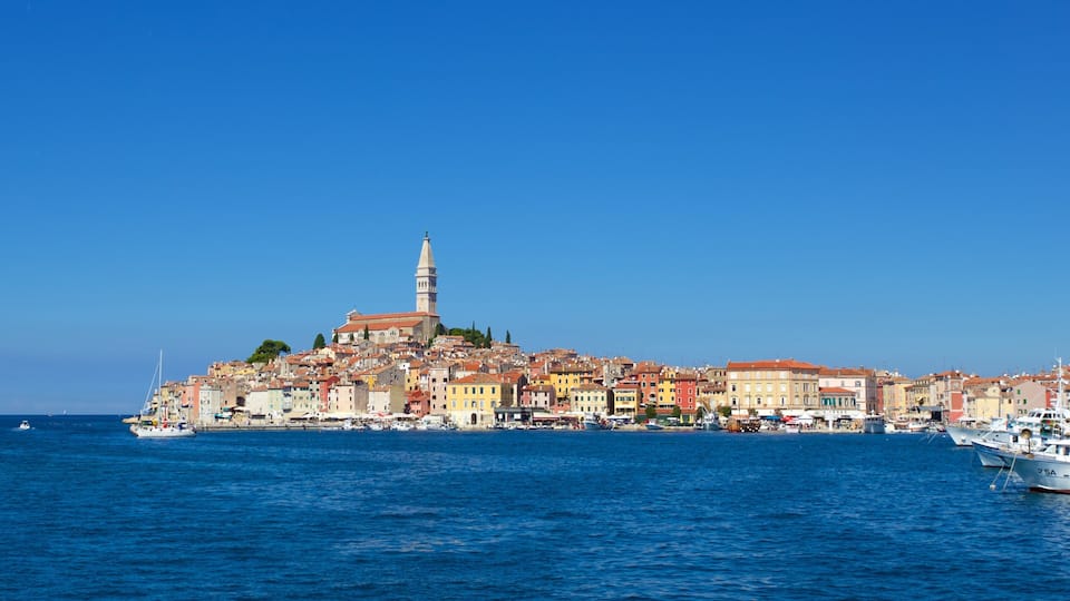 A coastal city with colorful buildings, a prominent tower, and boats in the harbor.