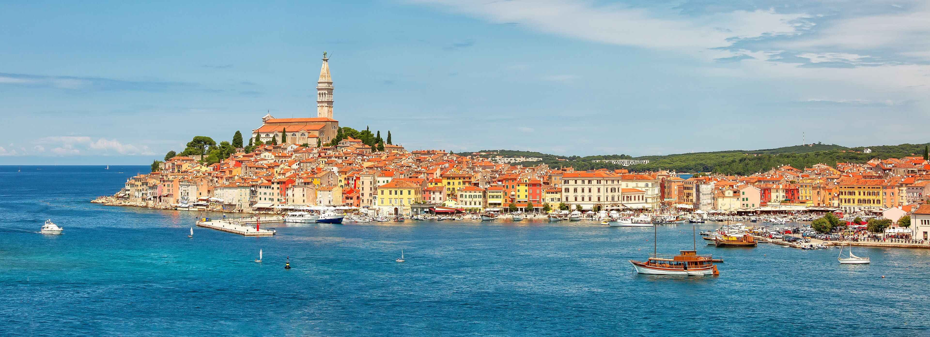 A coastal town with a prominent church and tower, colorful buildings, and boats on the water.