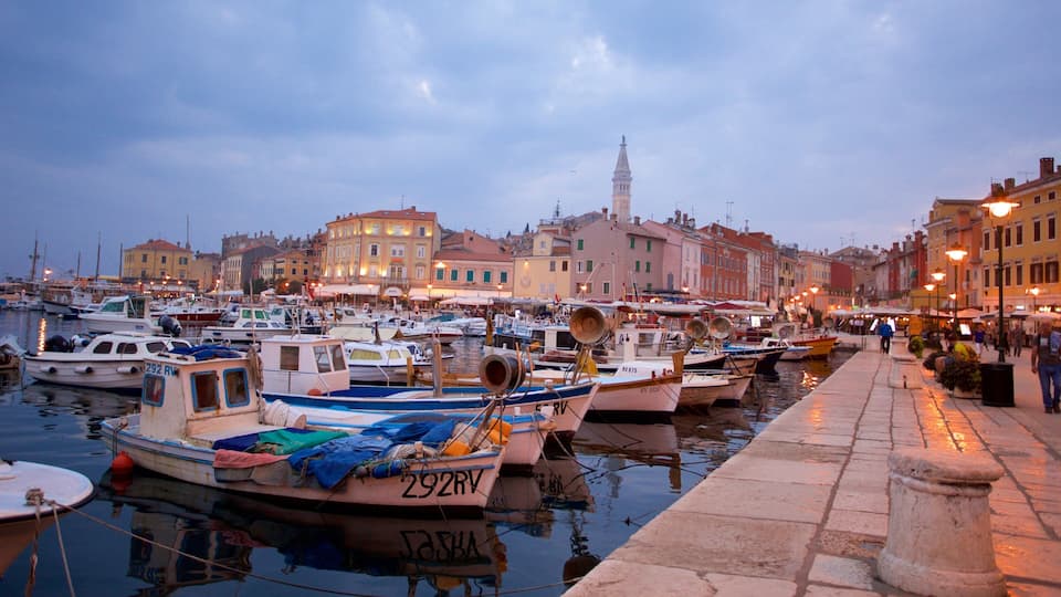 A marina with boats docked, a waterfront promenade, and historic buildings in the background.