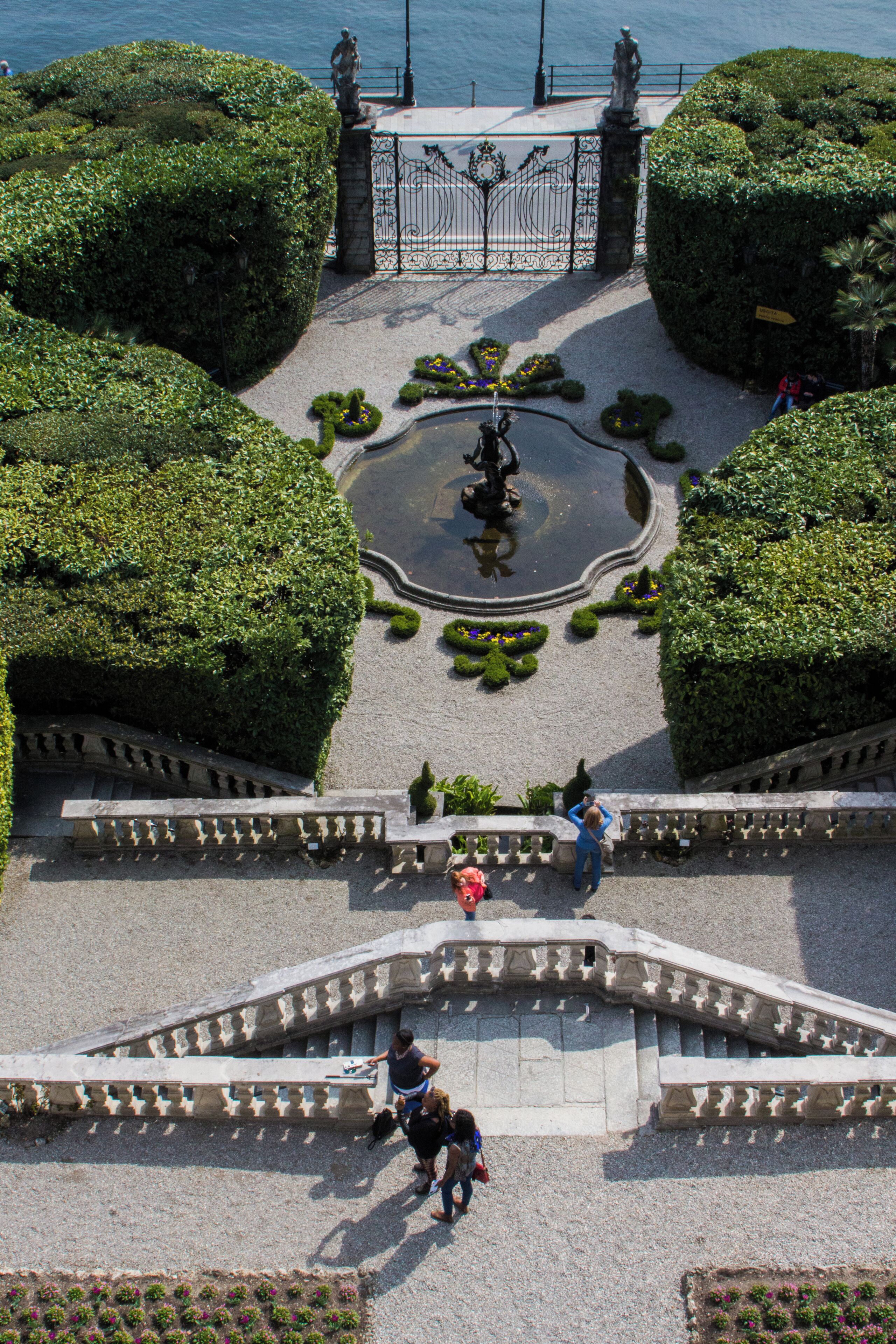 Um jardim paisagístico com uma fonte, estátuas e um caminho pavimentado.