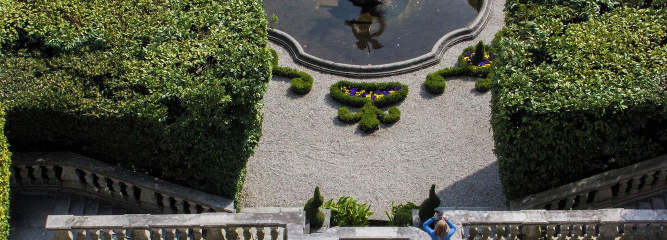Um jardim paisagístico com uma fonte, estátuas e um caminho pavimentado.