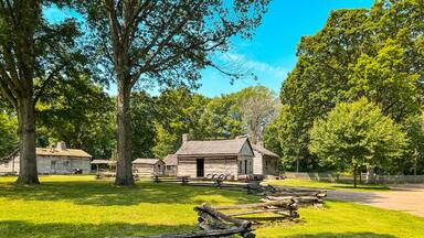 A historic log cabin surrounded by lush green trees and a wooden fence.