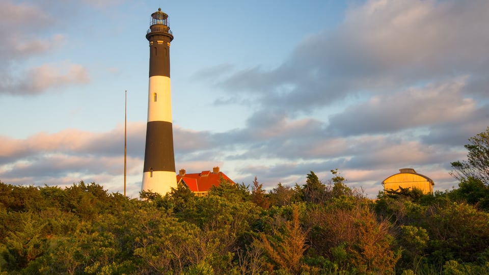 A lighthouse with a red roof, surrounded by dense greenery and a cloudy sky.