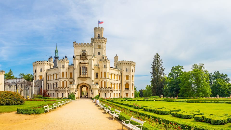 A grand castle with a flag, a well-manicured garden, and a clear sky.