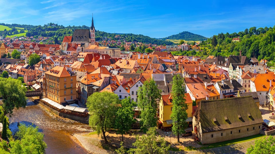 A historic town with a river, red-roofed buildings, and a prominent church spire.