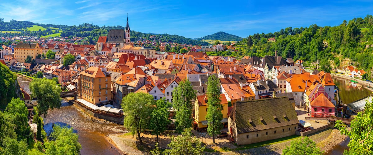 A historic town with a river, red-roofed buildings, and a prominent church spire.