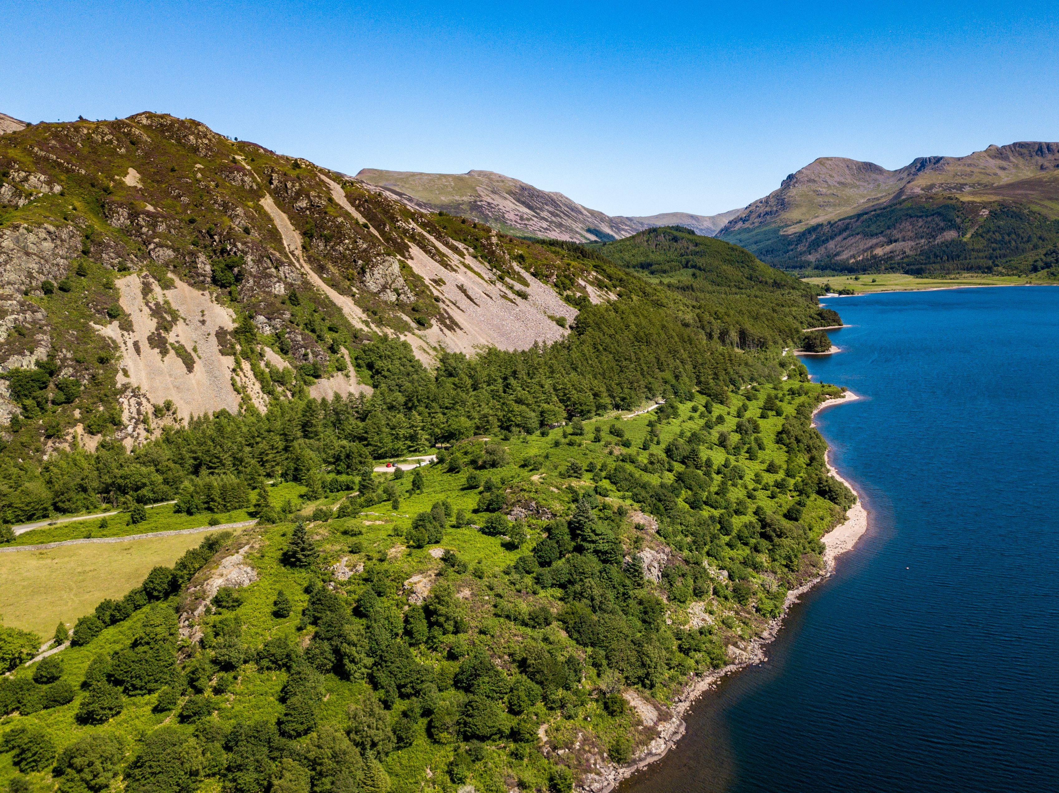 A mountainous landscape with a lake, dense forests, and a clear sky.