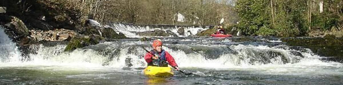 Ein Kajakfahrer bewegt sich auf einem Fluss, im Hintergrund ein Wasserfall.