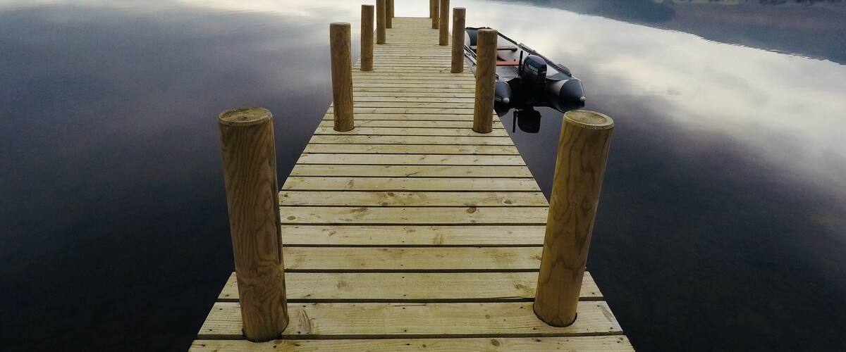 A wooden pier extending into calm water with a motorboat docked at the end.