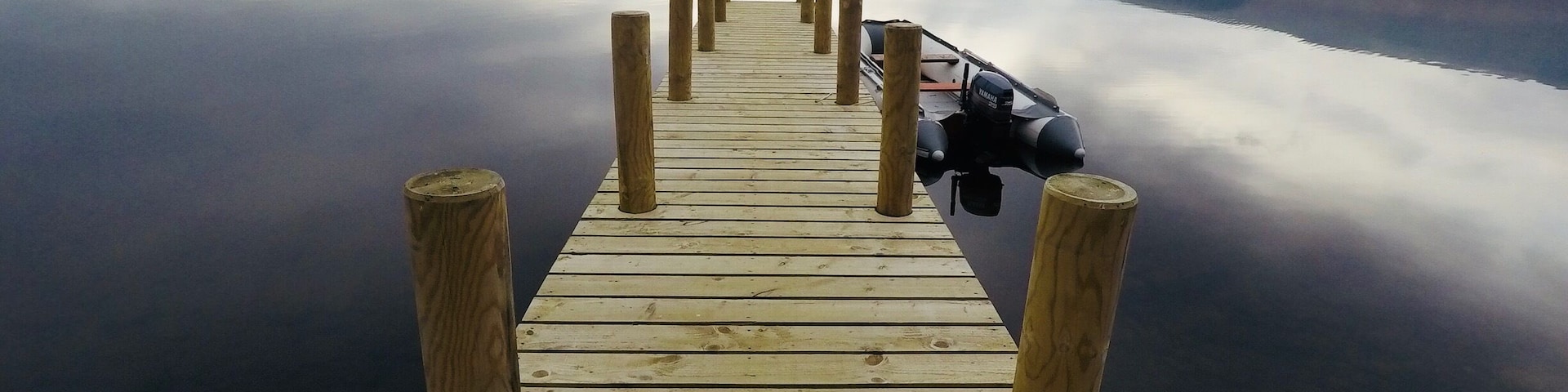 A wooden pier extending into calm water with a motorboat docked at the end.