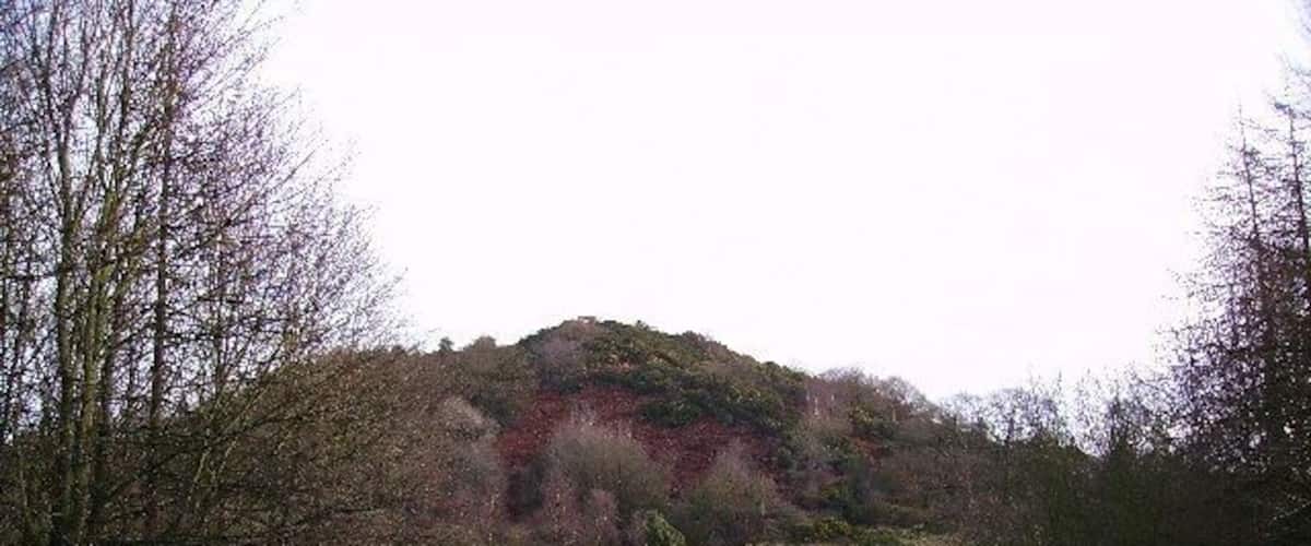 A winding road curving through a hilly landscape with sparse trees and a hill in the background.
