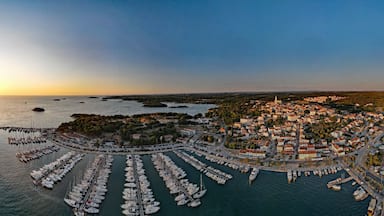 Un pueblo costero con un puerto deportivo lleno de barcos, una aguja de iglesia y un paisaje montañoso al fondo.