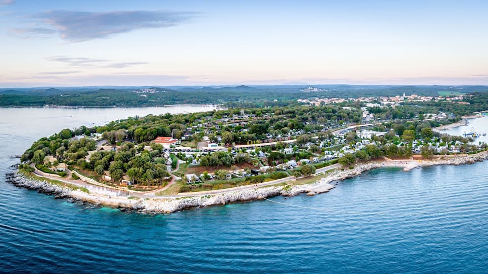 An aerial view of a coastal town with a central island surrounded by water, featuring residential areas, a marina, and a distant mountain range.