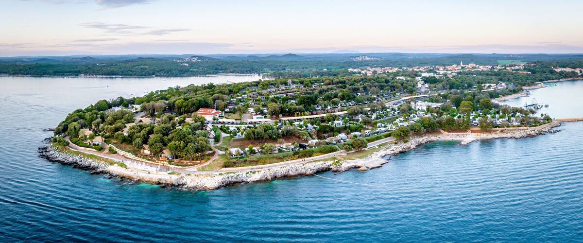 An aerial view of a coastal town with a central island surrounded by water, featuring residential areas, a marina, and a distant mountain range.
