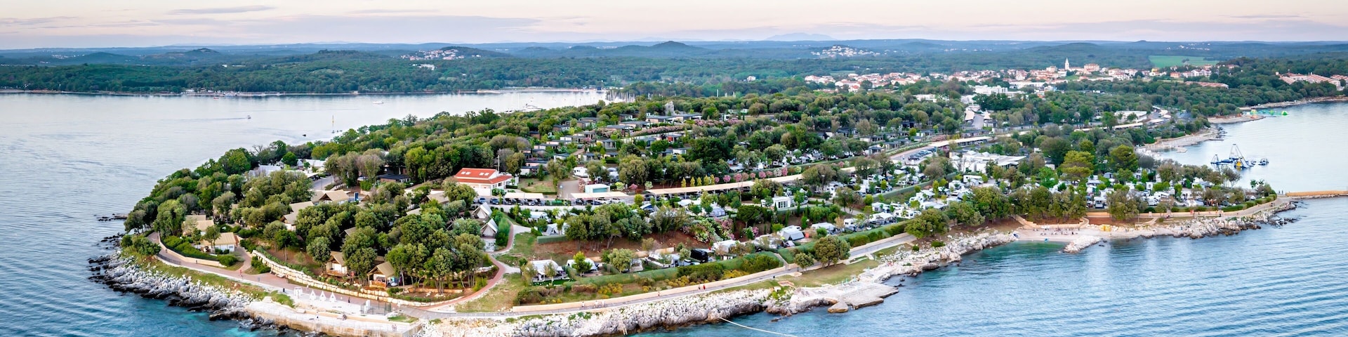 An aerial view of a coastal town with a central island surrounded by water, featuring residential areas, a marina, and a distant mountain range.