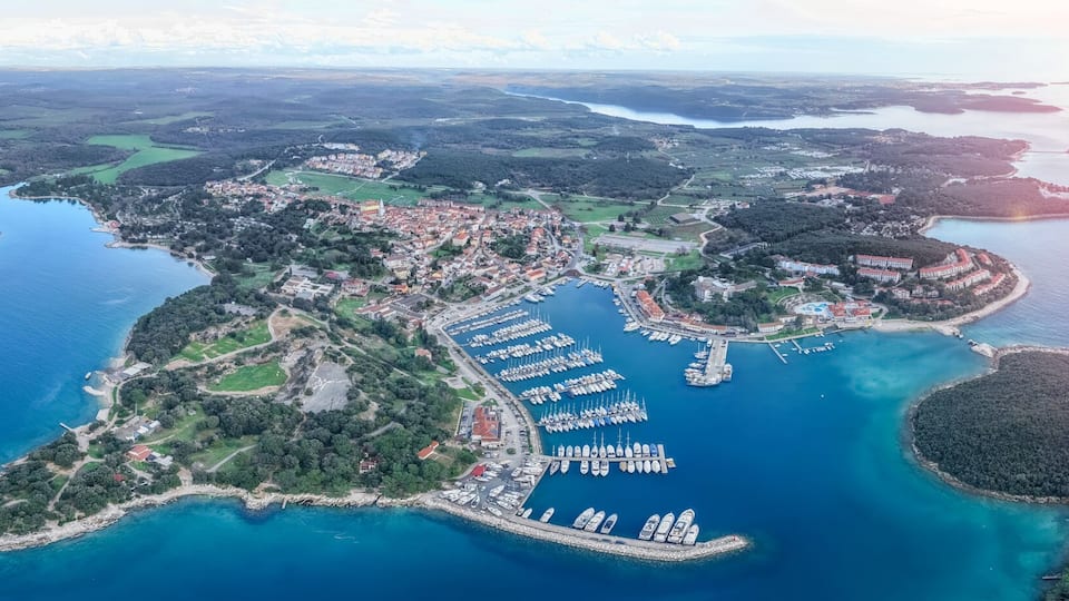 An aerial view of a coastal town with a marina, surrounded by islands and a large body of water.