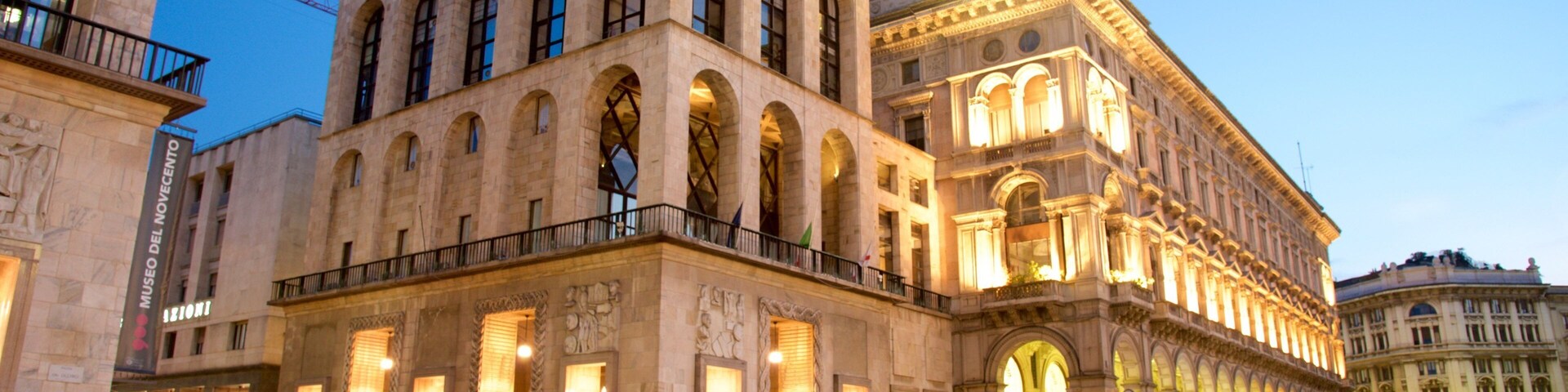 Un edificio histórico con ventanas de arco y un balcón, iluminado al anochecer.